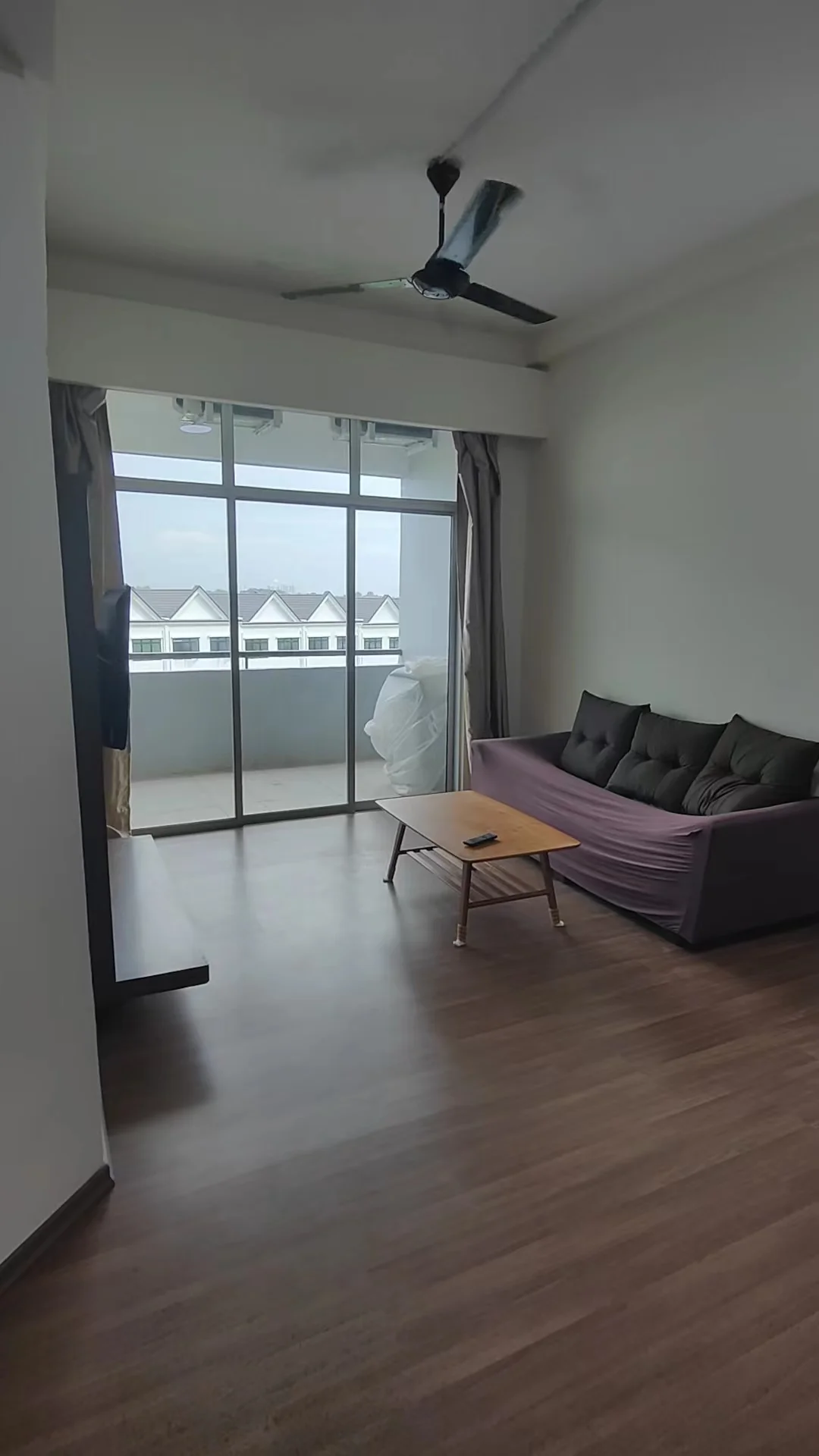Living features: 3-seater fabric sofa in dark grey, wooden coffee table, laminate flooring, floor-to-ceiling windows, sheer curtains, ceiling fan, balcony view, neutral painted walls; style: modern; view: city.